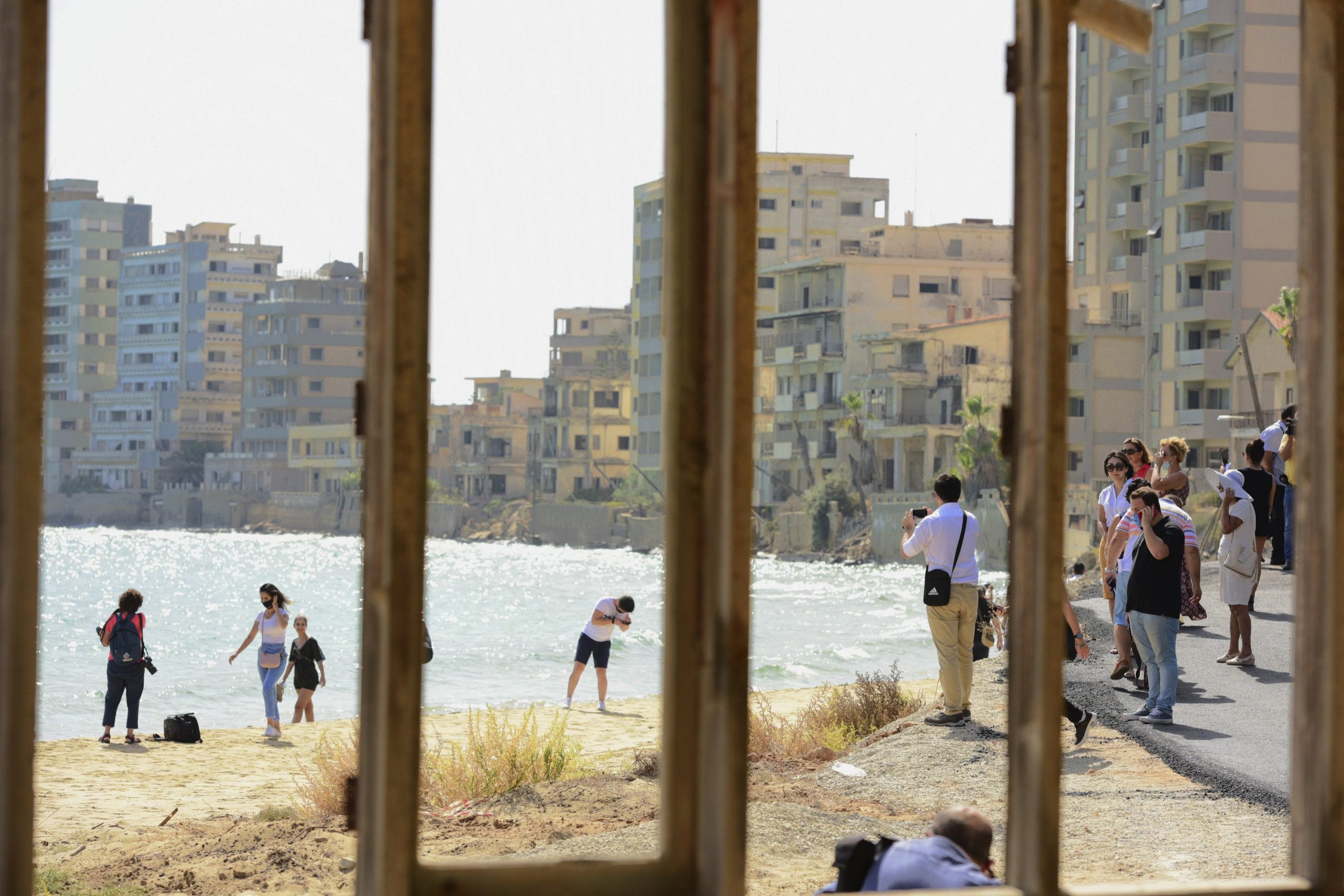 Journalists and the public are seen through a window frame at the beach lined with abandoned hotels, after the reopening of Varosha, in the fenced-off area of Gazimağosa (Famagusta), TRNC, Oct. 8, 2020. (AP Photo)