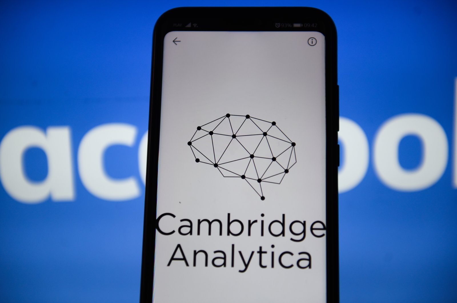 In this photo illustration, a Cambridge Analytica logo on a smartphone is held in front of a Facebook background, Sept. 24, 2019. (Photo by Getty Images)